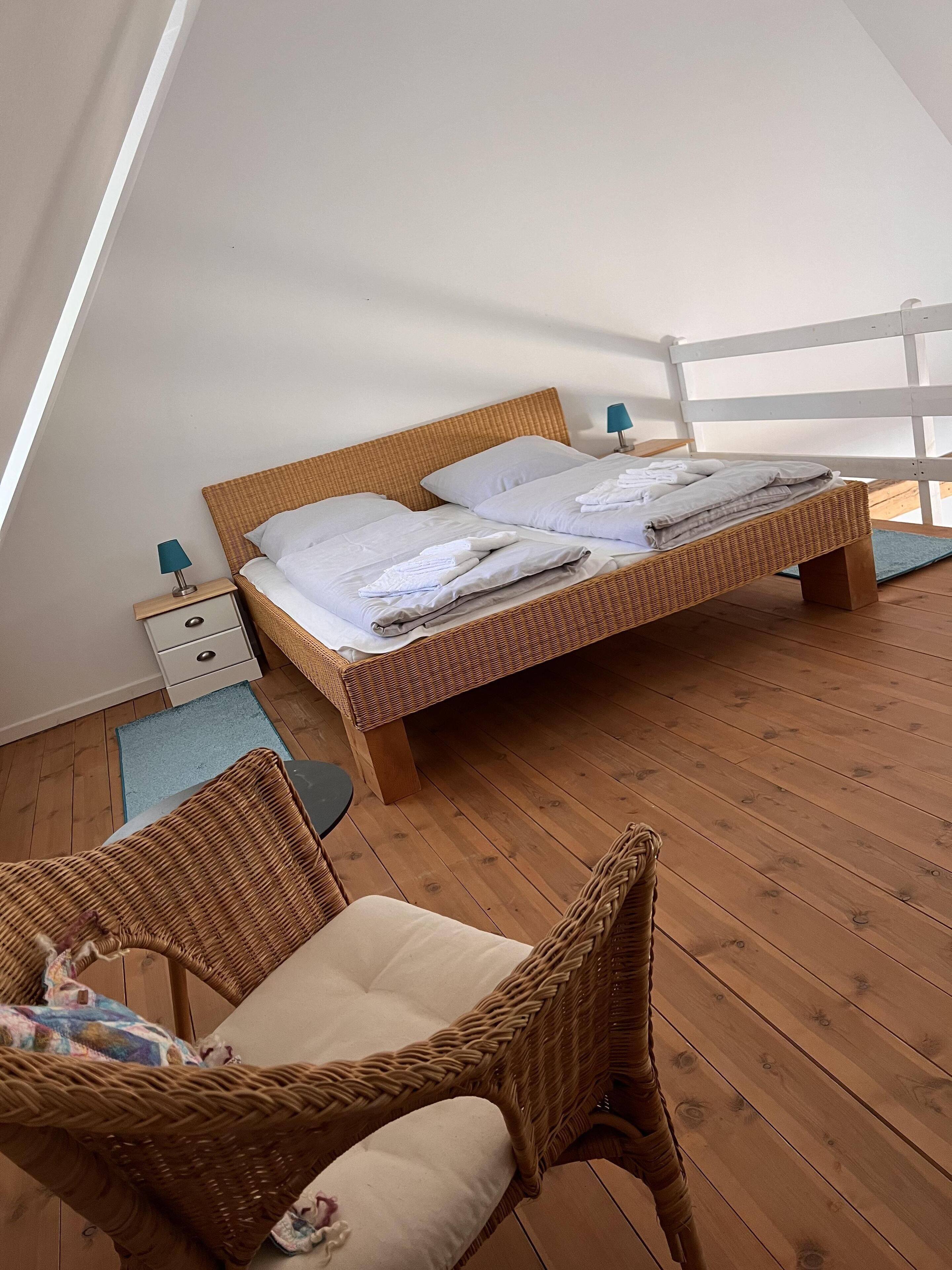Quarto com cama, mesa de cabeceira, cadeira e vista para o exterior.