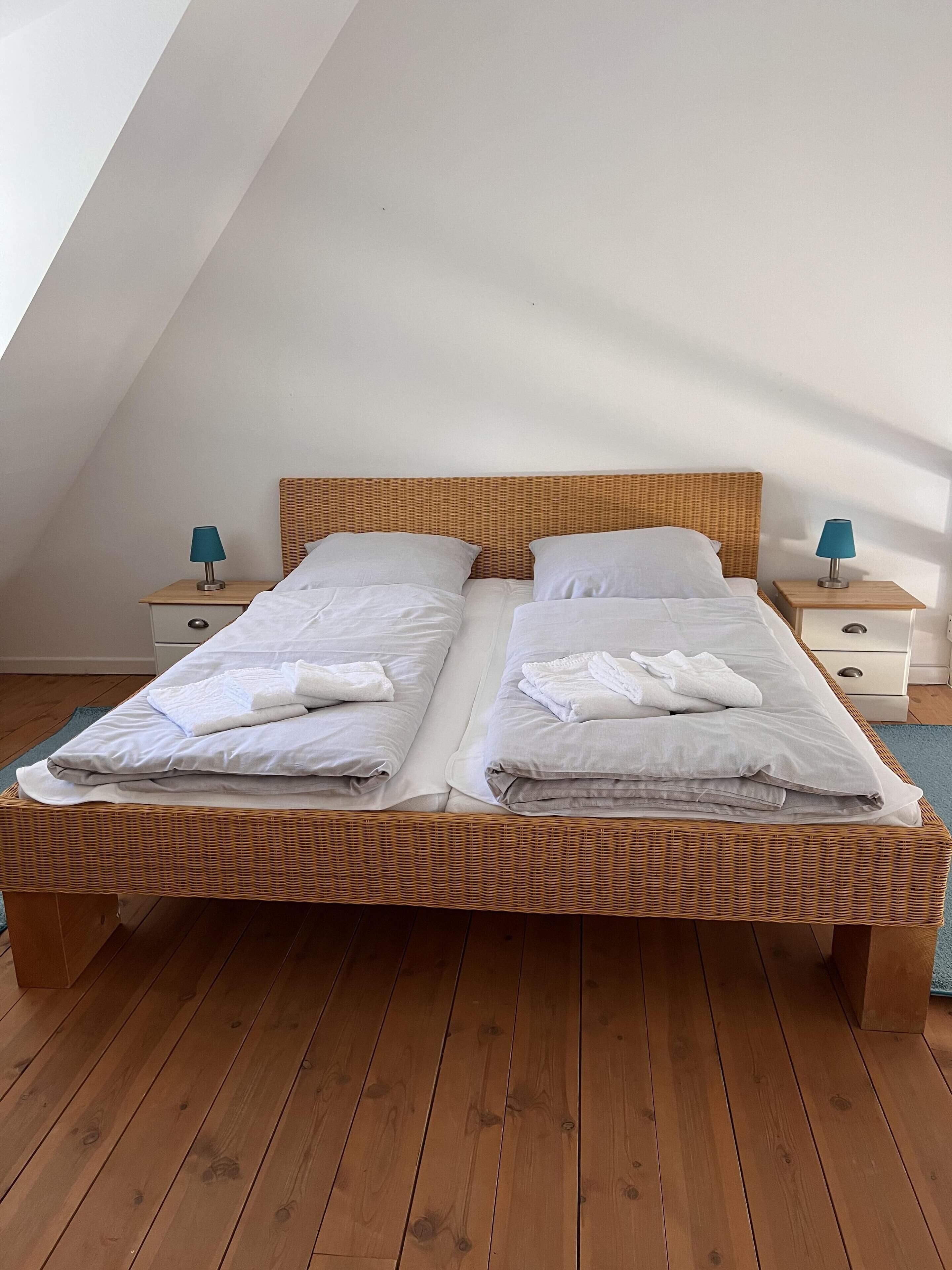 A double bed with white linens and towels, a wooden headboard, and two bedside tables with lamps.