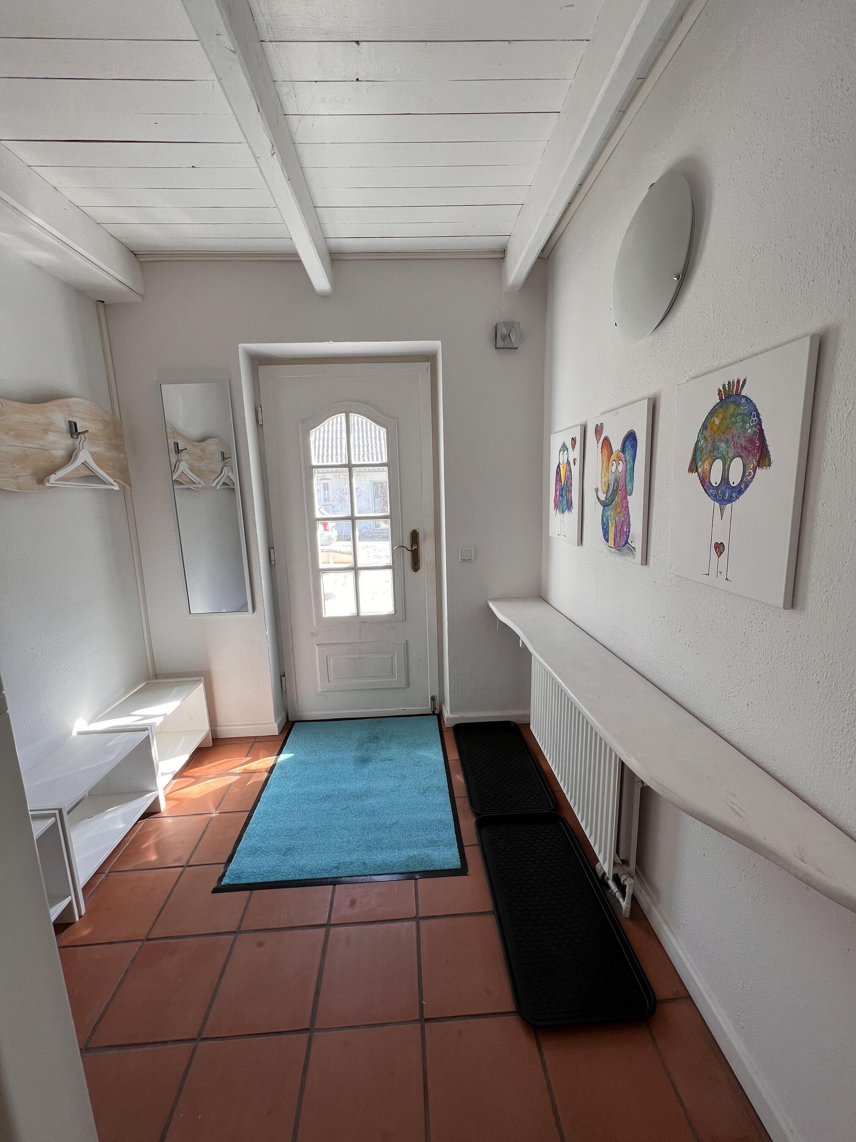 Un pasillo con una puerta blanca, un tapete azul, un tapete negro y obras de arte colgadas en la pared.