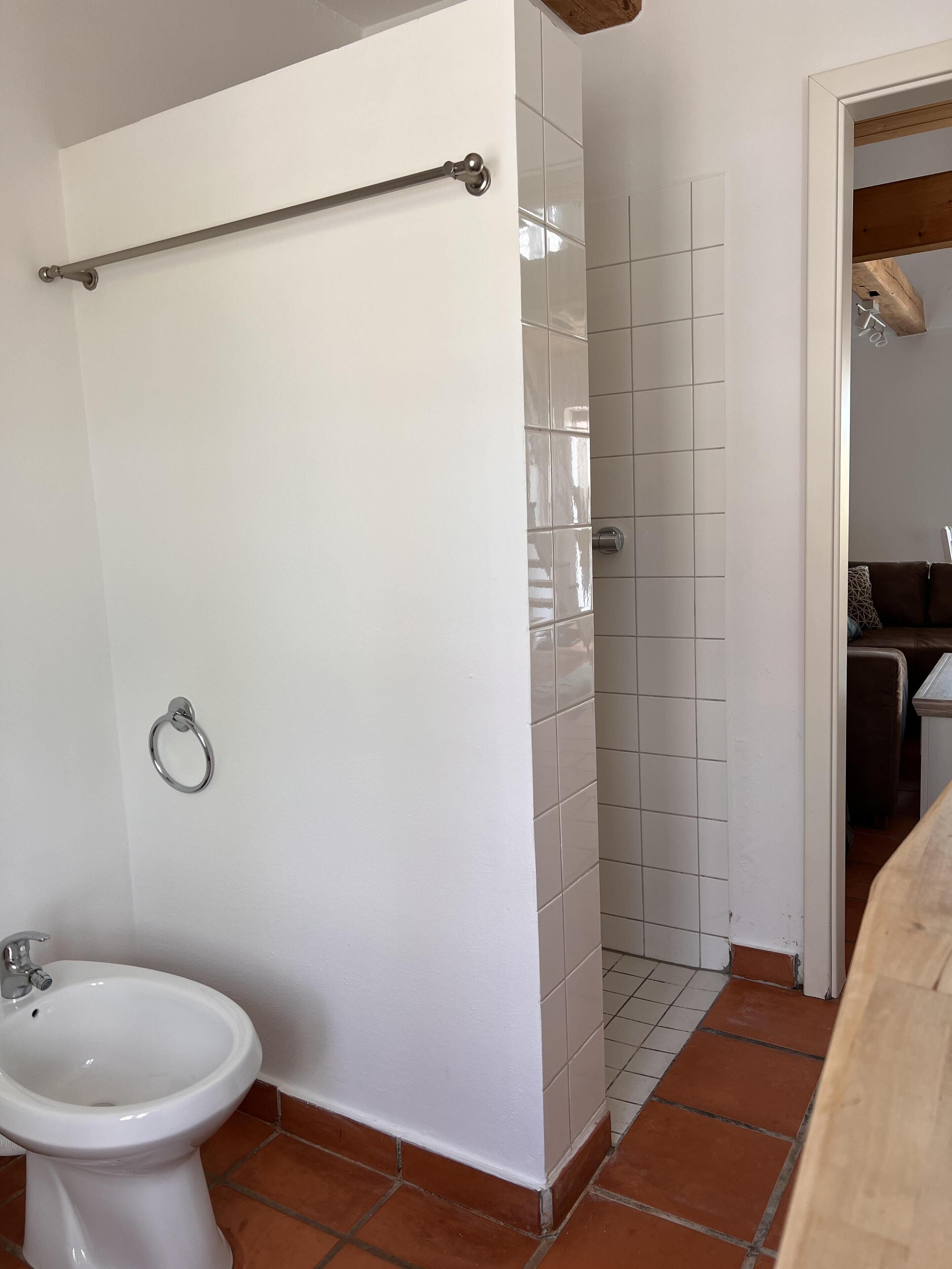 Une salle de bain avec des toilettes blanches, un bidet, un porte-serviettes et un espace douche aux carreaux blancs.