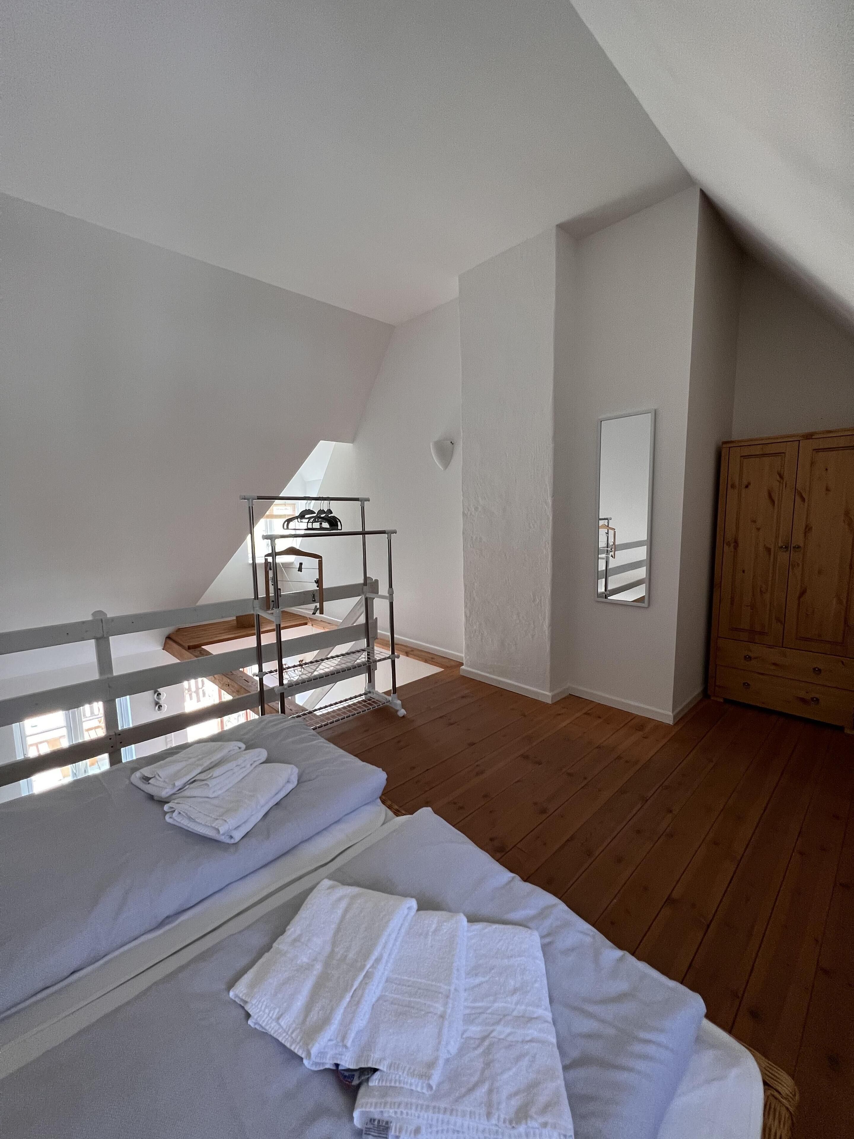 Ein Zimmer mit zwei Betten, einem Holzschrank, einem Spiegel und einem Oberlicht.