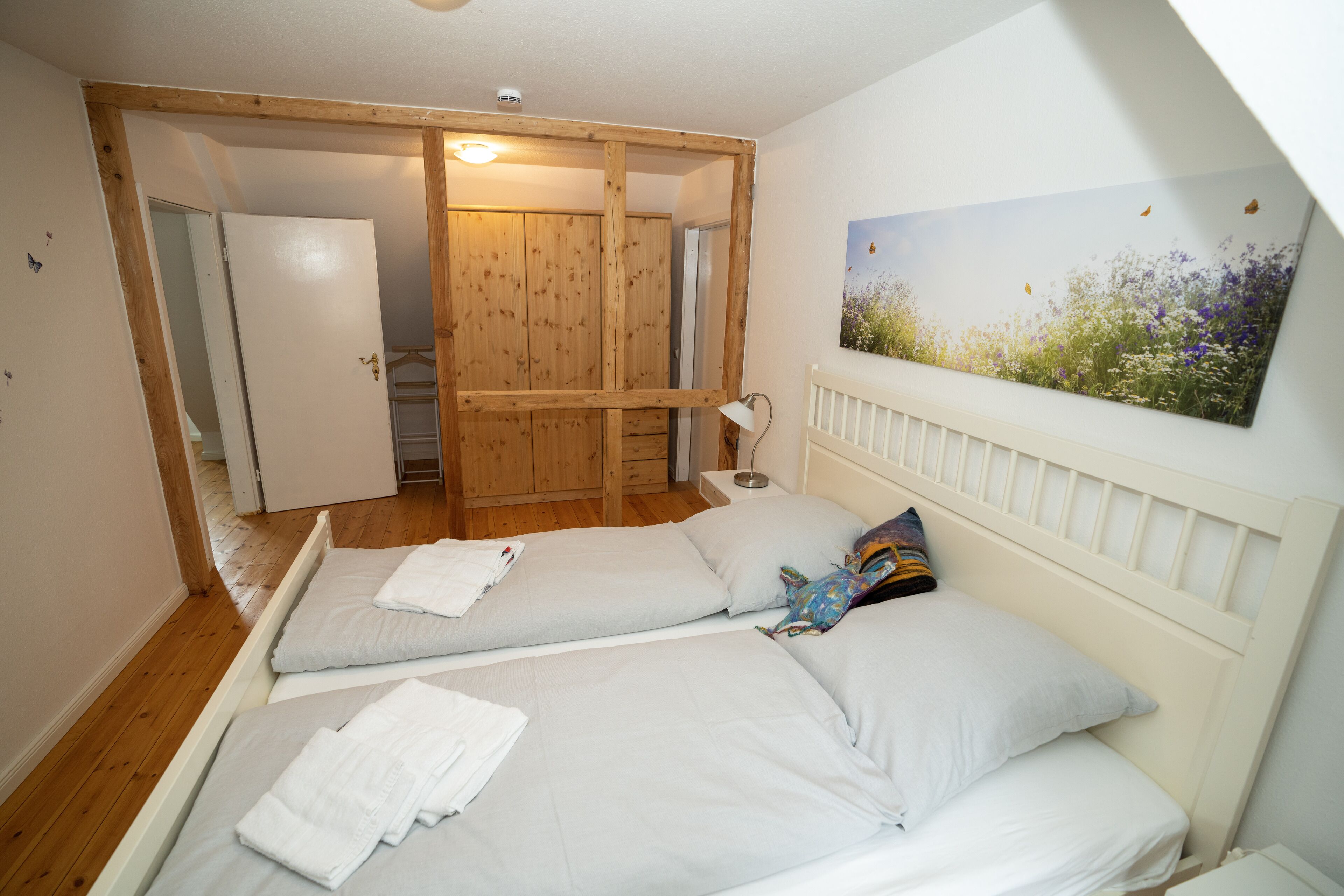 A bedroom with two beds, wooden wardrobe, and a painting on the wall.