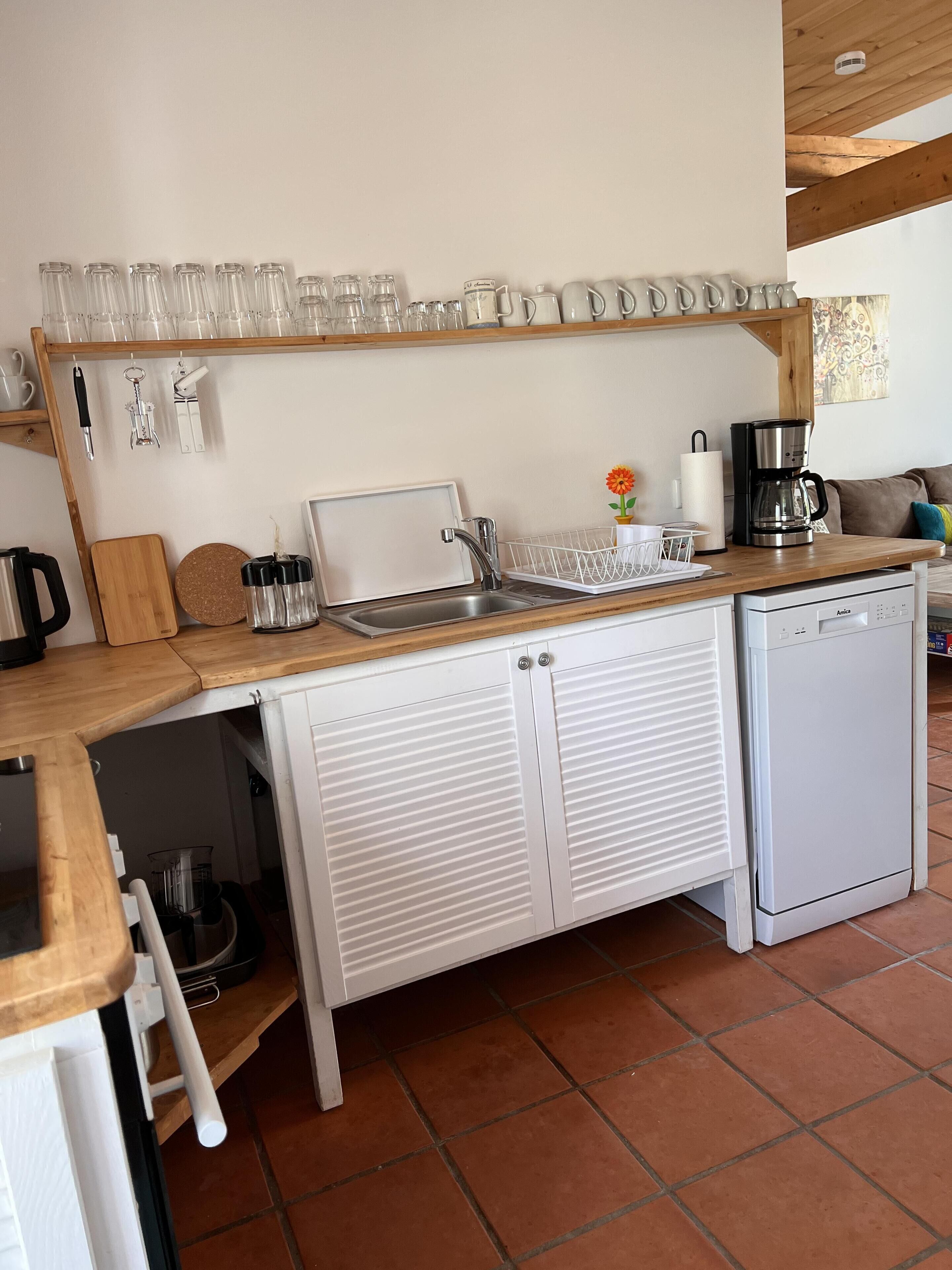 Een kleine keuken met een spoelbak, koffiezetapparaat en kastjes.