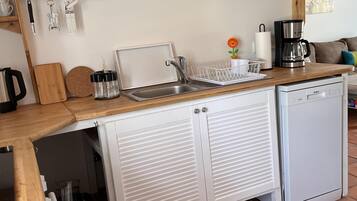 Een kleine keuken met een spoelbak, koffiezetapparaat en kastjes.