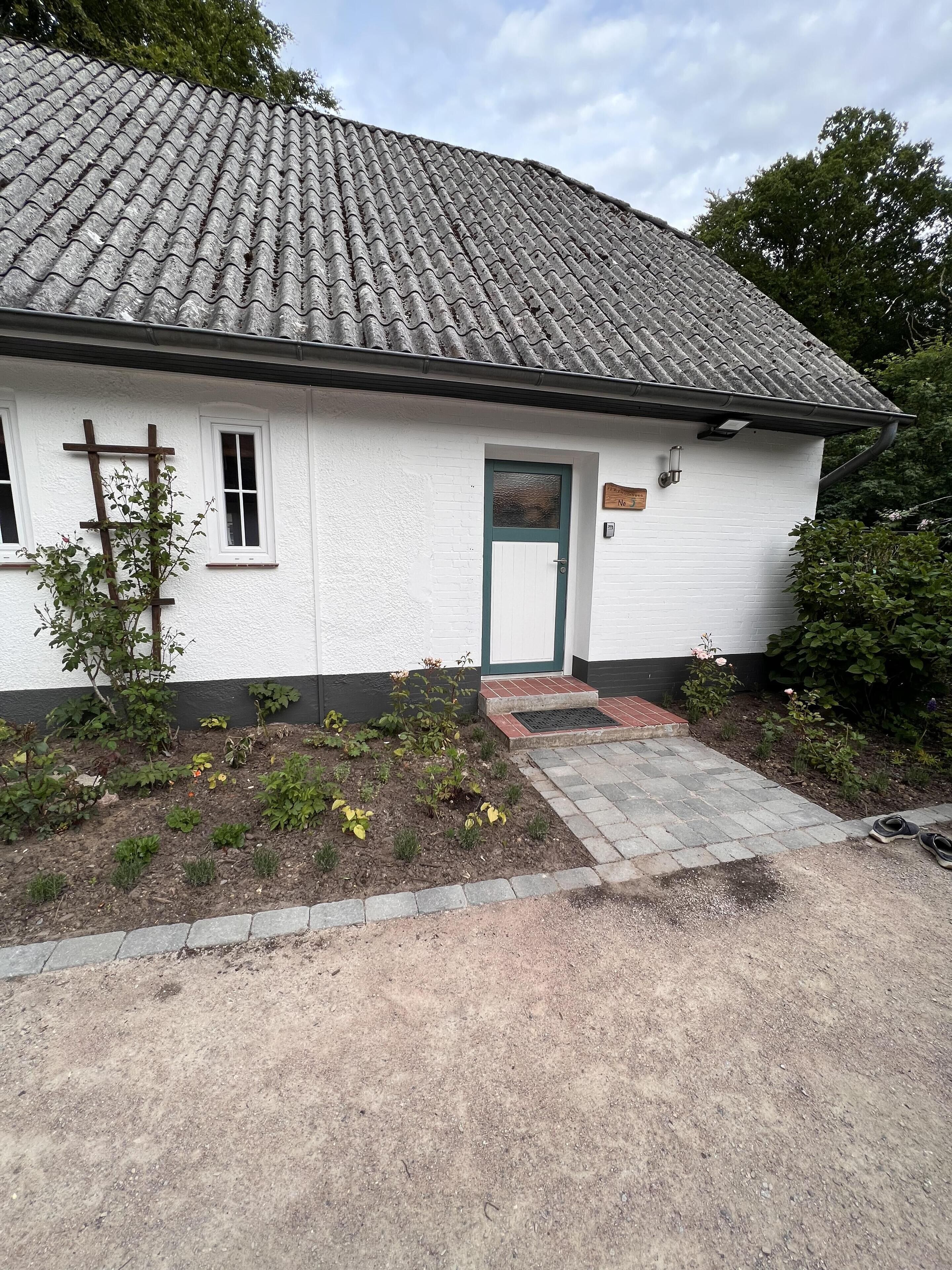 Een wit gebouw met een pannendak, een groene deur en een kleine tuin met planten en bloemen.