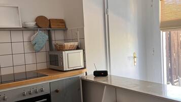 Una cocina con estufa, microondas y un estante con platos y recipientes.