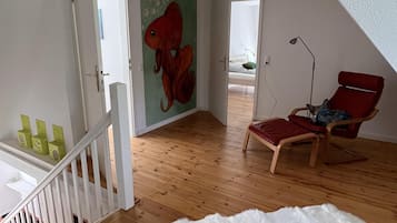 Una habitación amplia con piso de madera, una silla roja, un tapete blanco y mullido, y un mural de peces en la pared.
