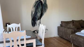 Ein Essbereich mit einem Holztisch und Stühlen, einer weißen Wand mit einem Vogelgemälde und einem braunen Ledersofa.