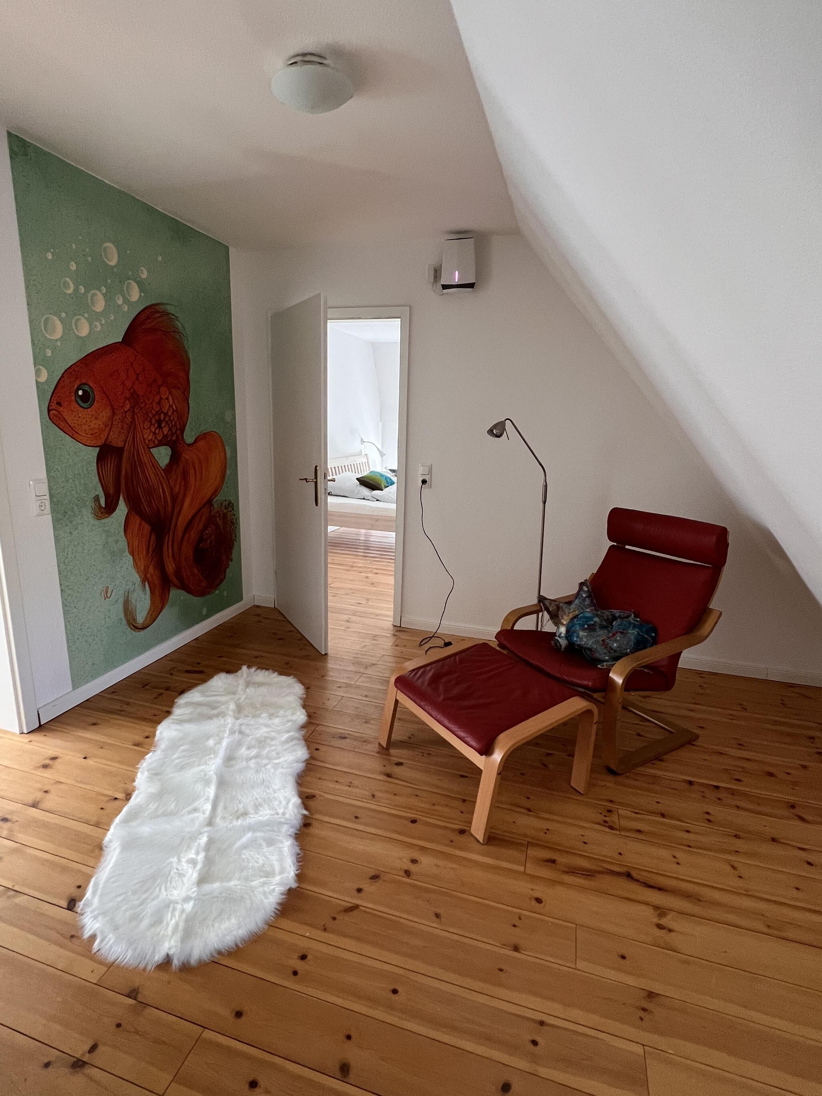 Een kamer met een houten vloer, een rode stoel, een wit, zacht tapijt en een muurschildering van vissen op de muur.