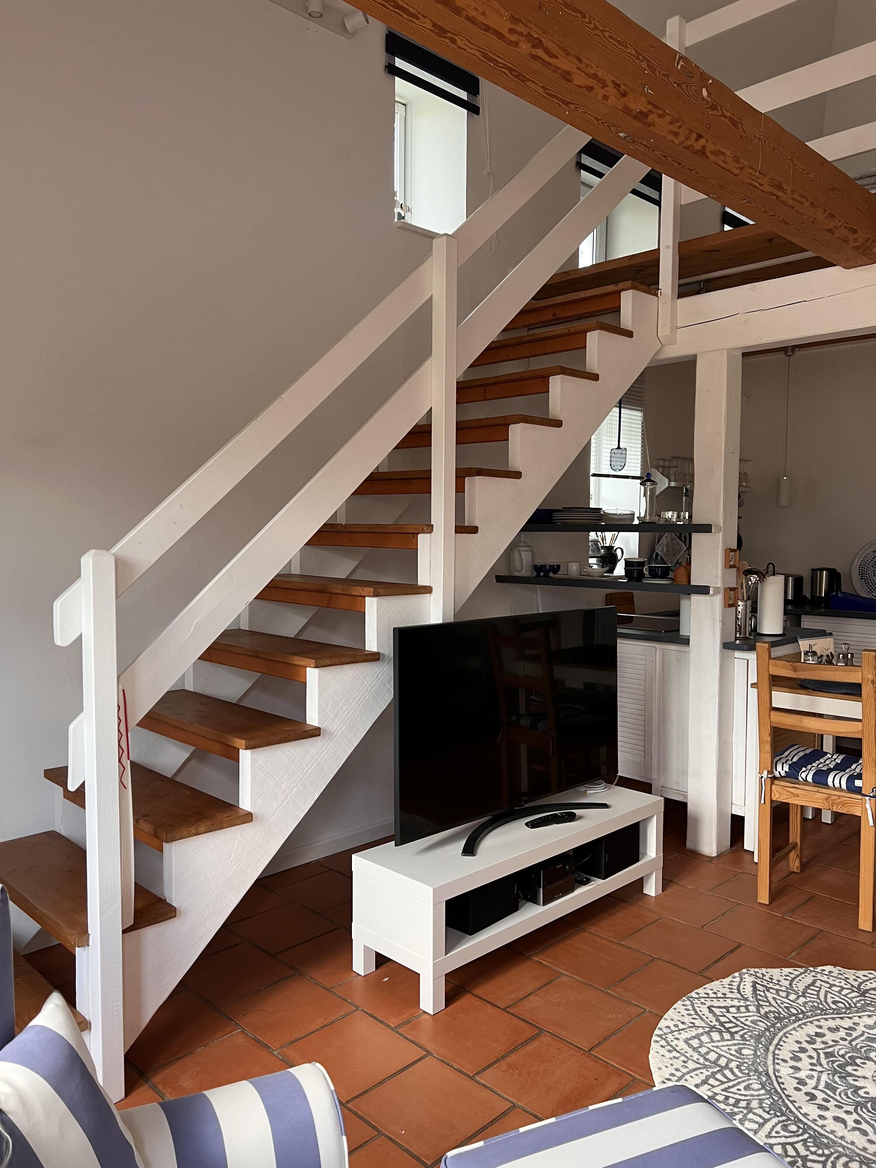 A staircase with wooden steps and white railings, leading to a kitchen area with a dining table and chairs.