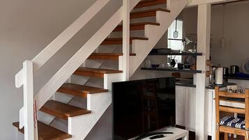 A staircase with wooden steps and white railings, leading to a kitchen area with a dining table and chairs.