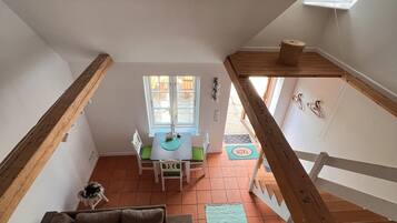 Une pièce confortable de style loft, avec un plafond en bois, un coin repas comprenant une table et des chaises, un canapé avec des coussins et un petit tapis sur le sol.