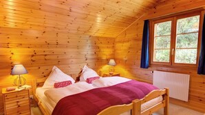 Ein Schlafzimmer einer Holzhütte mit einem Bett, zwei Nachttischen, Lampen und einem Fenster mit Vorhängen.