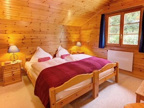 A wooden cabin bedroom with a bed, two bedside tables, lamps, and a window with curtains.