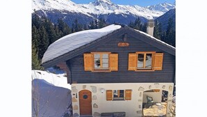 Ein Chalet mit Steinverkleidung, Holzläden und einem mit Schnee bedeckten Dach.