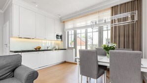 A modern kitchen with white cabinets, a dining area with a table and chairs, and a large window with curtains. - Happy Stay Sopot Monte Cassino 40 (Sopot)