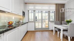 A modern kitchen with white cabinets, a granite countertop, and a dining area with a white table and grey chairs. - Happy Stay Sopot Monte Cassino 40 (Sopot)