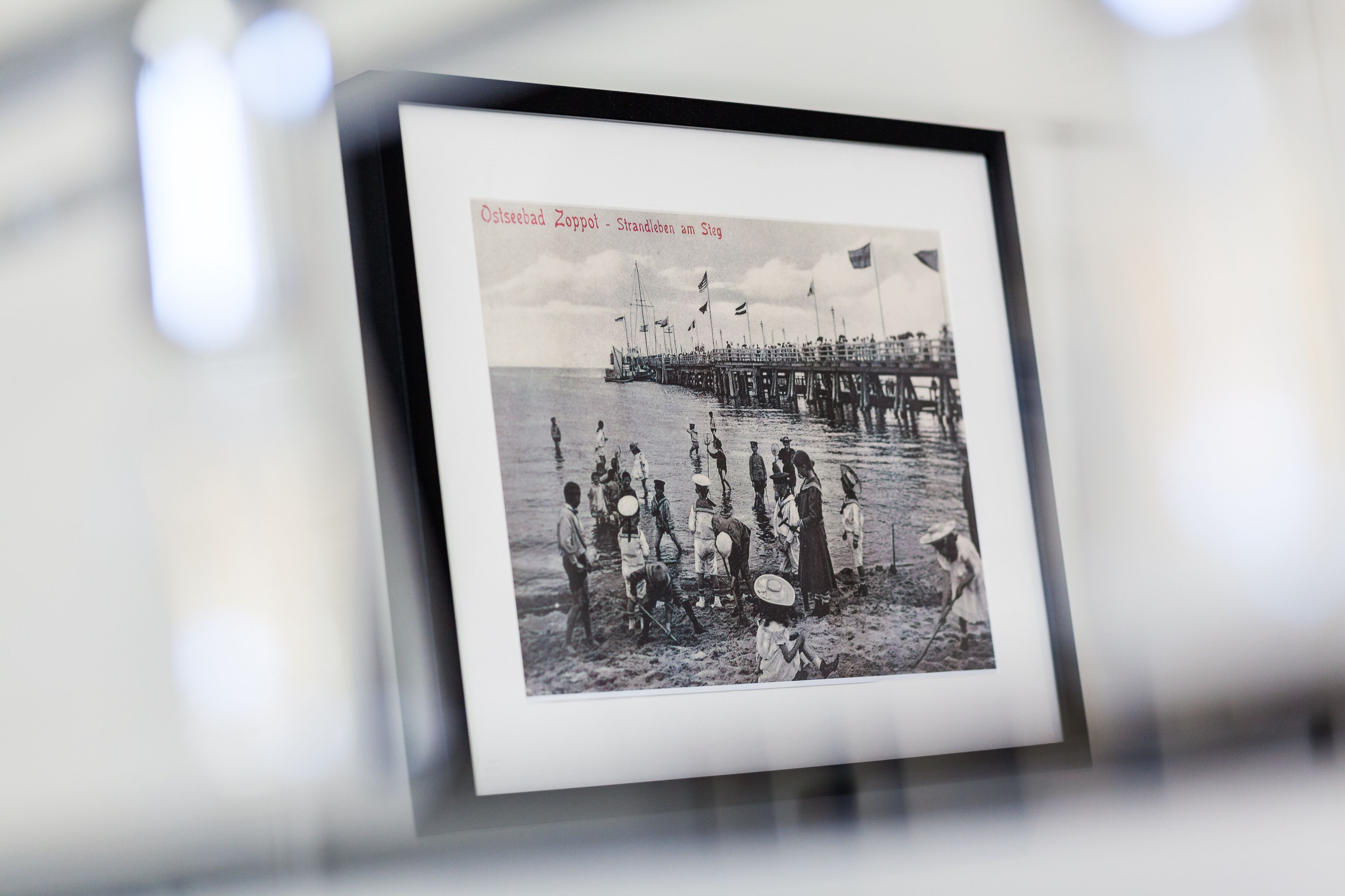A framed black and white photograph of a pier with people and a ship.