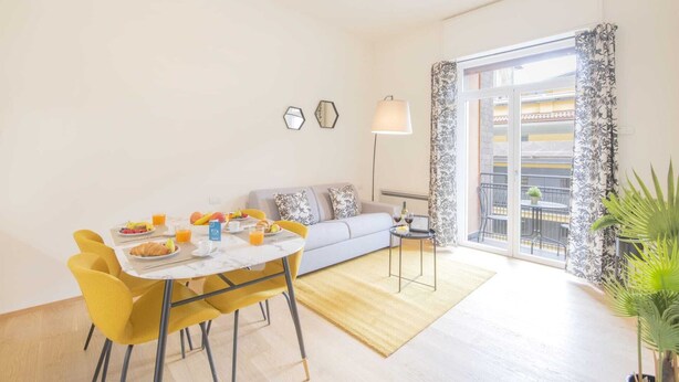 A modern living room with a dining area, a sofa, a coffee table, and a view of the outside balcony. - Sweett | Fancy Duomo I (Milano)