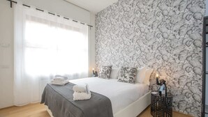 A bedroom with a bed, a nightstand, a lamp, and a wall with a leaf pattern. - Sweett | Fancy Duomo I (Milano)