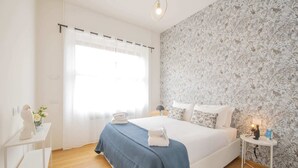 A bedroom with a large bed, a nightstand, a lamp, and a wall with a floral pattern.