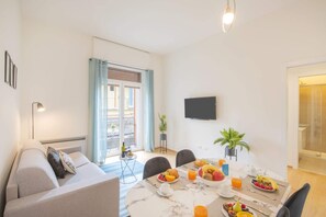 Een moderne woonkamer met een bank, een ontbijtstatafel en een televisie aan de muur, plus een balkon met uitzicht.