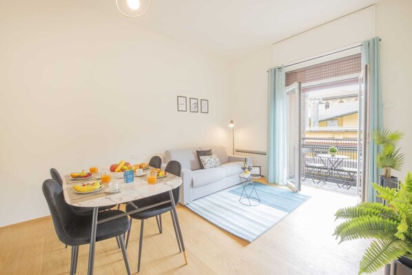 Un appartement moderne comprenant un coin repas, un canapé et un balcon aménagé avec du mobilier d’extérieur.