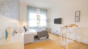 Une chambre à coucher moderne et bien éclairée, avec un lit, une table de chevet et un petit espace bureau.