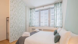 Een hotelkamer met een bed, kussens, een raam met gordijnen en een radiator.