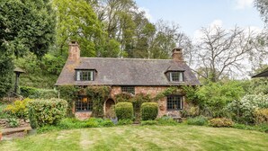 A stone house with a gabled roof, two chimneys, and a well-maintained garden with hedges and flowering plants. - Saint Pancras Chapel (Watchet)