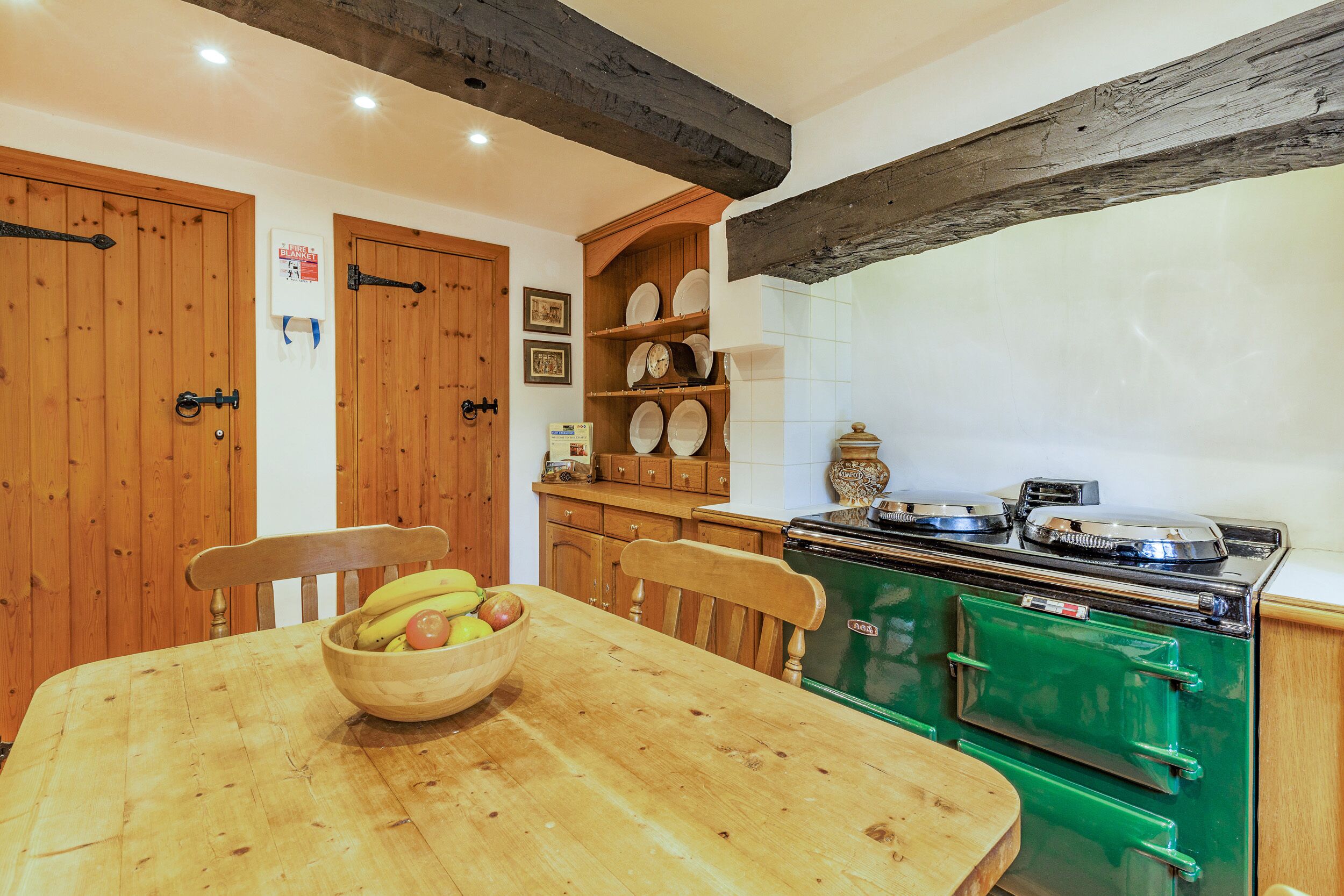 A kitchen with wooden cabinets, a green stove, and a wooden dining table with a bowl of fruit.