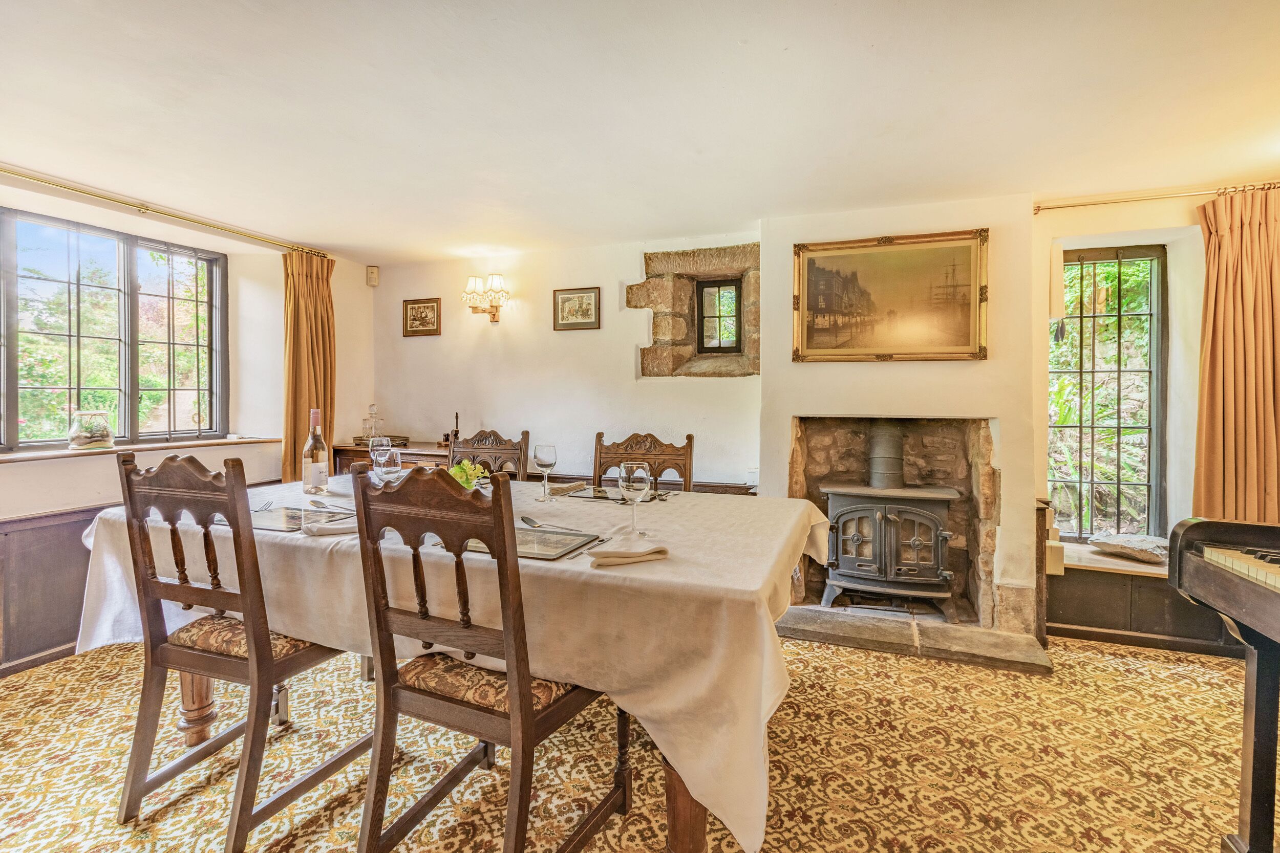 Une salle à manger avec une table dressée pour quatre personnes, une cheminée et une vue sur la verdure à l’extérieur.
