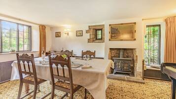 Une salle à manger avec une table dressée pour quatre personnes, une cheminée et une vue sur la verdure à l’extérieur.
