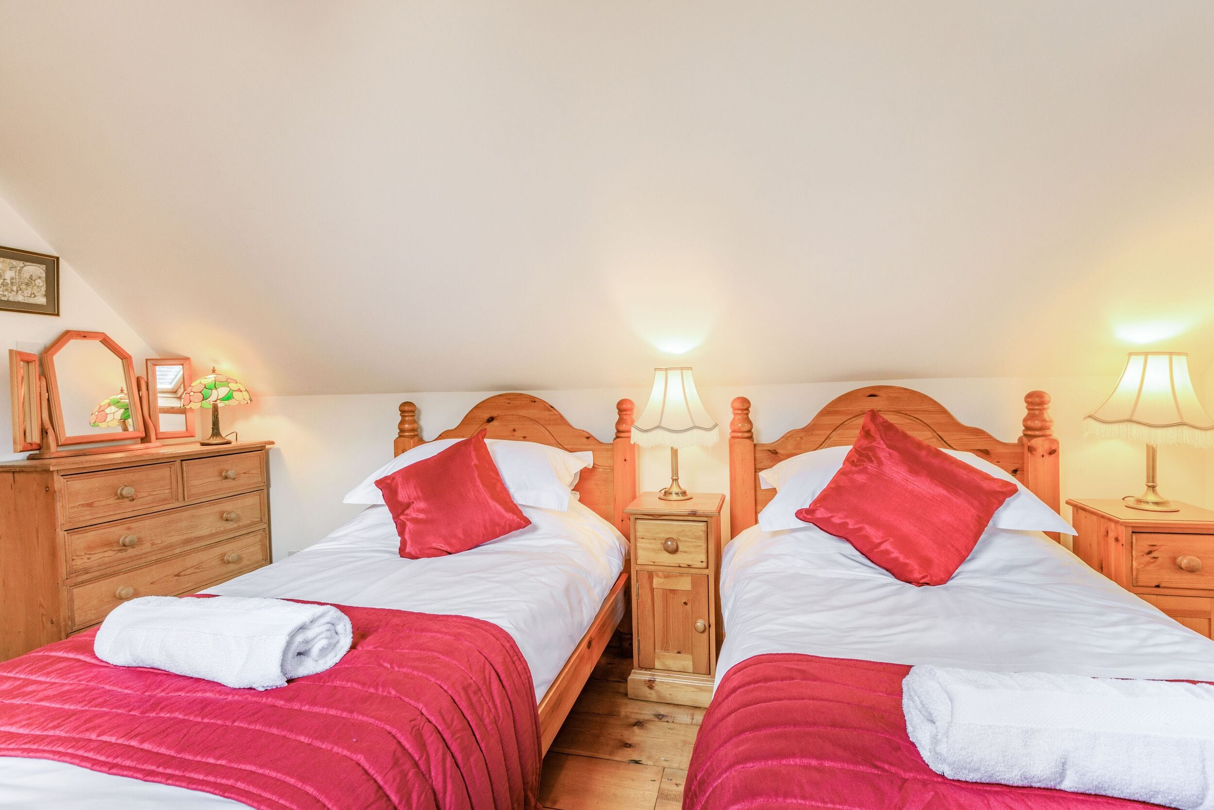 Ein Doppelzimmer mit zwei Betten, Holz-Kopfteilen, Nachttischen mit Lampen und einer Holzkommode.