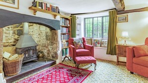 A cozy room with a stone fireplace, a red armchair, a bookshelf, and a window with a view of greenery. - Saint Pancras Chapel (Watchet)