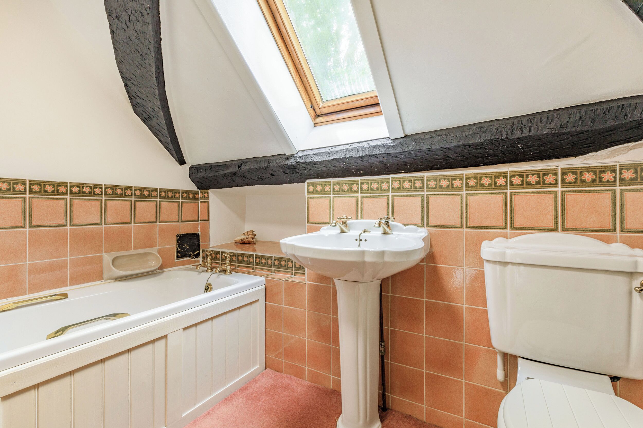Un baño con tragaluz, bañera, lavamanos pedestal y retrete.