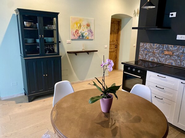 A modern kitchen with a wooden table, white chairs, a dark cabinet, and a tiled backsplash.