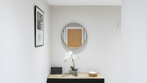 Un couloir minimaliste avec une console noire, un tableau encadré, un miroir et une orchidée en pot.