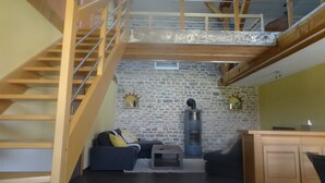 A loft-style living area with a wooden staircase, stone wall, and a fireplace. - Spacious, well-equipped, in a breathtaking setting (Mournans-Charbonny)