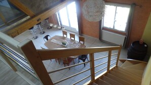 A dining area with a table and chairs, a hanging light fixture, and a staircase leading to another level. - Spacious, well-equipped, in a breathtaking setting (Mournans-Charbonny)