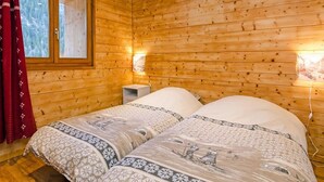 A wooden cabin room with two beds, a nightstand, and a window with curtains. - Chalet, wifi, sauna, balcony, parking, tv, ski locker, 230m², Peisey-Vallandry (Peisey-Nancroix)