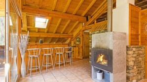 A rustic wooden interior with a stone fireplace, wooden ceiling beams, and a bar area with stools. - Chalet, wifi, sauna, balcony, parking, tv, ski locker, 230m², Peisey-Vallandry (Peisey-Nancroix)