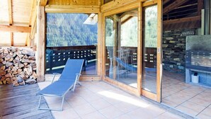 A wooden cabin with a patio area featuring two lounge chairs, a stone fireplace, and a view of a mountainous landscape. - Chalet, wifi, sauna, balcony, parking, tv, ski locker, 230m², Peisey-Vallandry (Peisey-Nancroix)