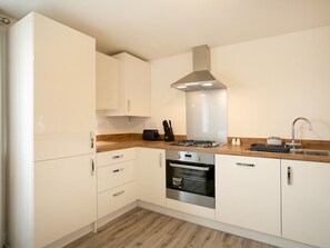 A modern kitchen with white cabinets, a stainless steel range hood, a built-in oven, and a wooden countertop.