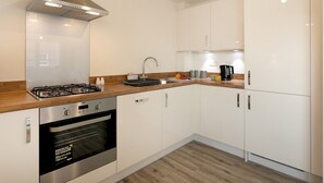 Une cuisine moderne avec des armoires blanches, une hotte de cuisinière en acier inoxydable, un four encastré et un plan de travail en bois.