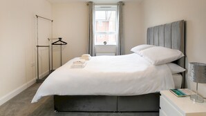Une chambre à coucher moderne avec un grand lit, une table de chevet avec une lampe et une vue sur l’extérieur par une fenêtre.
