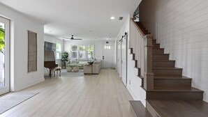 A spacious living area with a piano, a sofa, and a dining table. A staircase with wooden steps leads to another level.