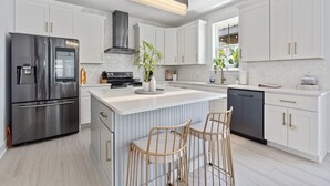A modern kitchen with white cabinetry, a stainless steel refrigerator, a central island with bar stools, and a built-in oven.