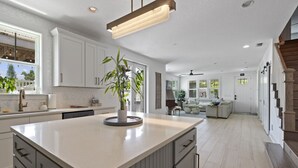 A spacious kitchen with a large island, white cabinetry, and a modern pendant light.