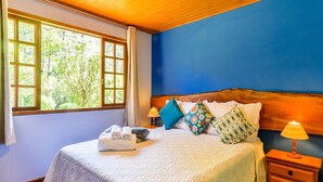 A bedroom with a large bed, a wooden headboard, a nightstand with a lamp, and a window with curtains. - Amadamata Refúgio Ecológico (Nova Friburgo)